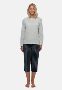 Grå langærmet top og marineblå stribede capribukser. Stoffet ser blødt ud; bukserne har lodrette hvide striber. Fødderne er bare.