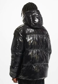 Zwarte pufferjack met een glanzende, gewatteerde afwerking, voorzien van een capuchon en elastische manchetten. De jas heeft een losse, oversized pasvorm en een ronde vorm.