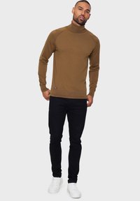 Bruine coltrui van een gladde breiselstof, met ribbelmanchetten en -zoom. Gecombineerd met slim-fit zwarte jeans en witte sneakers.