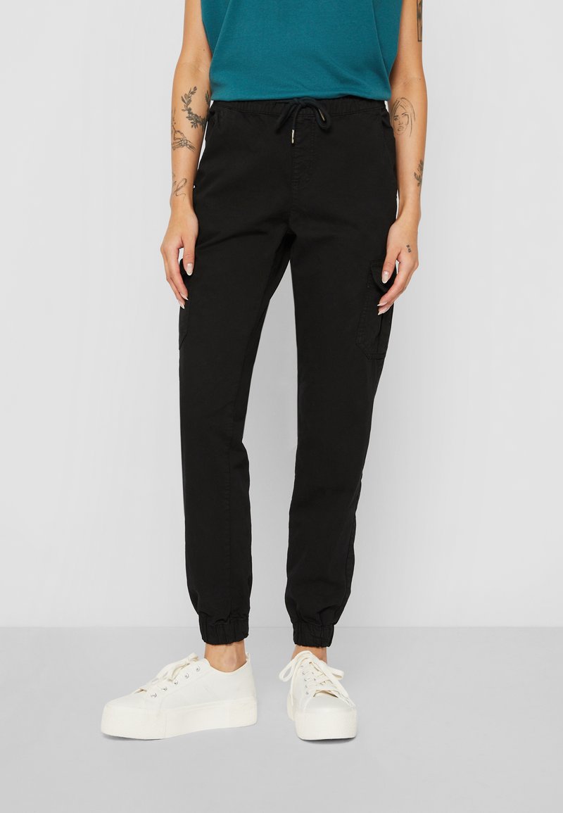 Svarta joggerbyxor i ett lätt material med elastiska muddar och dragsko i midjan. Har sidofickor. Matchas med vita sneakers.