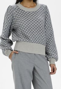 Hellgrauer Pullover mit einem strukturierten blauen Muster, Rundhalsausschnitt und gerippten Bündchen. Kombiniert mit hellgrauen, lässigen Hosen.