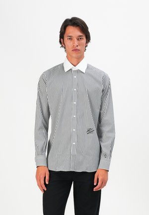 Striped button-up shirt with black and white vertical stripes, a white collar, and a small logo detail on the lower front.