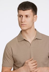 Polo beige con colletto classico e maniche corte, caratterizzato da una sottile trama e una vestibilità morbida.