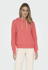 Sudadera de color coral con un bolsillo frontal, cordones dorados y un pequeño bordado de corazón dorado en el lado izquierdo del pecho. Tela suave y casual.