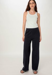 Donkerblauwe wijde broek met een gladde textuur en voornaden, gecombineerd met een lichtgrijze tanktop. Schoeisel is een paar grijze instapsandalen.