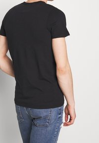 Camiseta de algodón negra de manga corta con cuello redondo, diseño ajustado y textura suave, combinada con jeans azules desgastados.
