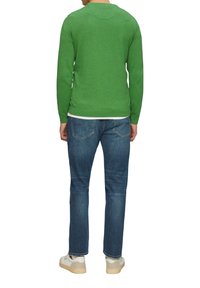 Groene gebreide trui met een ronde halslijn en lange mouwen, gecombineerd met blauwe spijkerbroek. De spijkerbroek heeft een klassiek 5-pocket ontwerp.