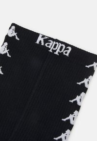 Svarte ribbede sokker med hvit "Kappa"-logo og gjentatte hvite silhuetter av en person langs sidene.