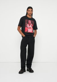 Camiseta de algodón negra con un gráfico rojo de un jugador de baloncesto en el frente, combinada con unos vaqueros negros de corte ancho y zapatillas negras.