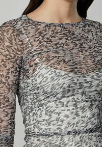 Top trasparente a maniche lunghe con motivo leopardato in tonalità di marrone e grigio, con una silhouette aderente e texture arricciata.