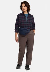 Kariertes Hemd in Dunkelblau und Burgunderrot, kombiniert mit braunen Hosen und einer blauen Bauchtasche. Schwarze Schuhe runden den Look ab.