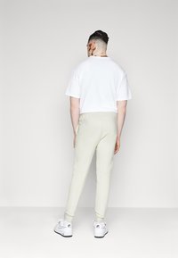 Ljust grå sweatpants med avsmalnande ben, en vit t-shirt och vita sneakers. Outfiten har en avslappnad passform och enkelt design.