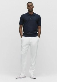 Mörkblå polotröja med korta ärmar, tre knappar i halslinningen, i kombination med vita byxor och vita sneakers, med en jämn tygtextur.