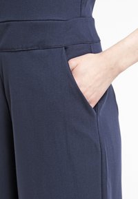 Prenda de color azul marino con una tela suave, corte recto y un bolsillo lateral, con una mano parcialmente visible dentro del bolsillo.