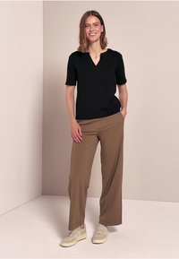 Schwarzes kurzärmeliges Oberteil mit V-Ausschnitt, kombiniert mit lockeren khakifarbenen Hosen und beigen Turnschuhen. Einfaches Design, minimale Details.