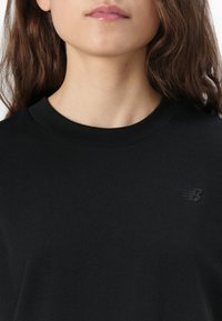 T-shirt en coton noir avec un col rond et un logo en relief discret sur la poitrine gauche. Texture lisse, design minimaliste.