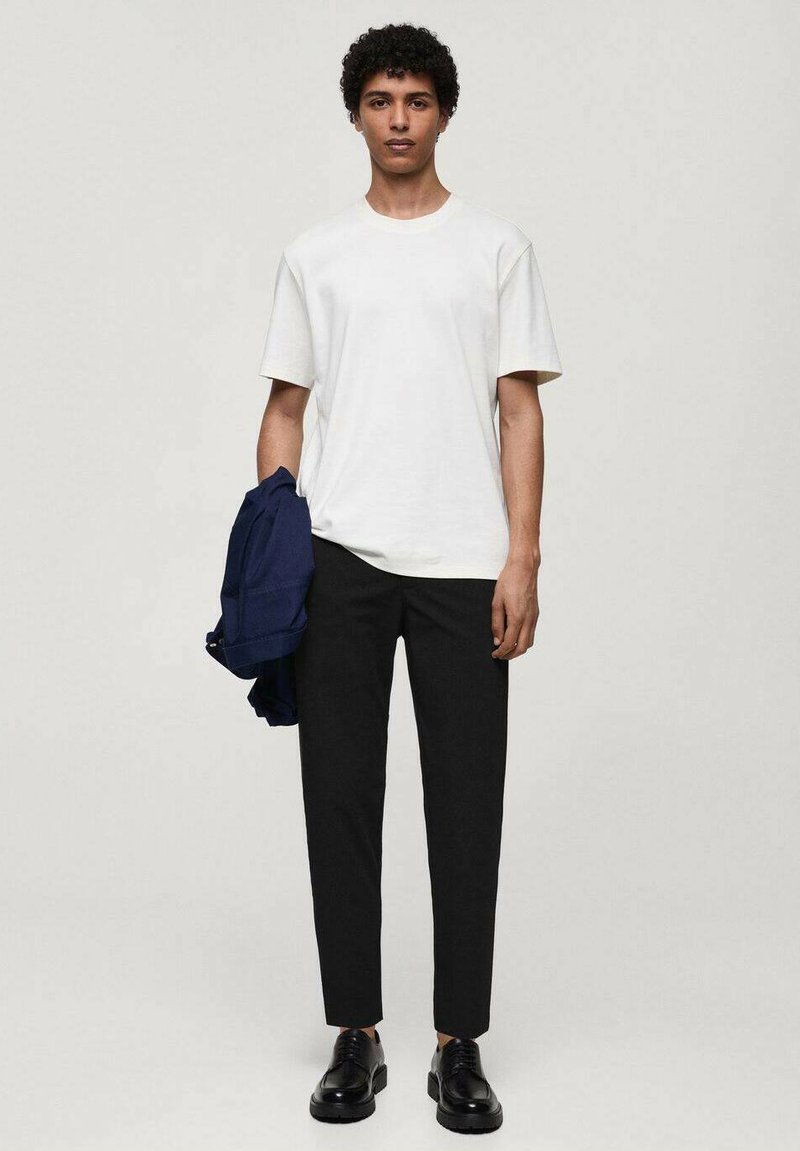 T-shirt blanc à manches courtes, pantalon noir fuselé, veste bleu marine drapée sur le bras, chaussures noires, tissu lisse, coupe décontractée, design minimaliste.
