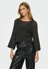 Pull en maille noire à coupe ample, avec un ourlet en dentelle et des manches évasées. Associé à un pantalon en faux cuir noir taille haute.