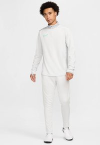 Hvid Nike langærmet top med en kvart-zip krave, der har et lysblåt logo. Sammen med matchende slim-fit bukser og sko med sorte detaljer.