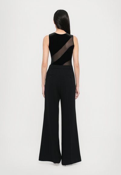 Black sleeveless bodysuit with sheer mesh accents, paired with high-waisted black wide-leg trousers, featuring back pockets.