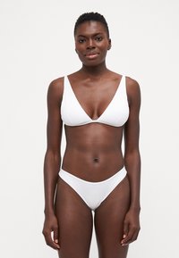 Baltas bikinis, kuriame yra trikampio formos liemenėlė su plačiomis petnešėlėmis ir žemais šortais. Lygus audinys ir minimalistiškas dizainas.