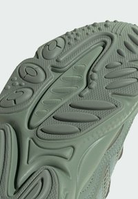 Podeszwa buta sportowego w jasnym zielonym kolorze, wykonana z gumowego materiału, z teksturowanymi wzorami, rowkami i zaokrąglonymi akcentami zapewniającymi przyczepność.