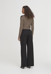 Sorte brede bukser med elastisk talje, parret med en langærmet top i brun og sort med striber og tætsiddende design.