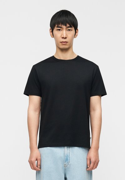 Μαύρο κοντομάνικο T-shirt από μαλακό βαμβάκι με στρογγυλή λαιμόκοψη, διαθέσιμο σε άνετη γραμμή και ίσια τελείωμα. Φοριέται με ανοιχτόχρωμο μπλε τζιν.