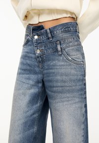 Vaqueros de tiro alto en azul claro, hechos de denim, con un ligero desgaste, dos bolsillos frontales y detalles metálicos en los botones.