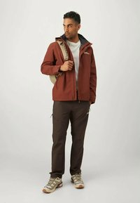 Αδιάβροχο μπορντό μπουφάν με μαύρο γιακά, γκρι πουκάμισο, καφέ παντελόνι και μπεζ ορειβατικά παπούτσια, κρατούσε μια μπεζ πλάτης στον έναν ώμο.