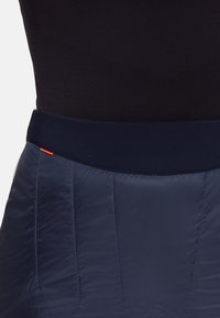 Mörkblå puffkjol med en slät yta, med ett fast midjeband och en orange accent vid sömmen. Vadderad design för isolering.