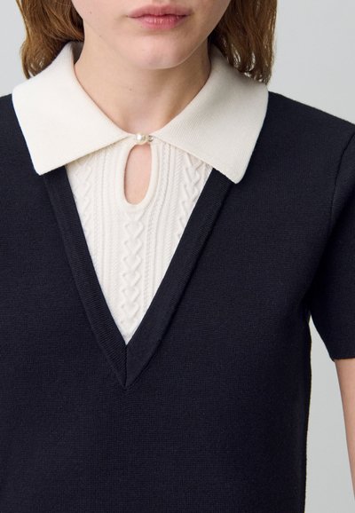 Abito lavorato a maglia con base blu navy, presenta un colletto bianco, dettaglio a chiave con accentatura in perla e un pannello testurizzato di colore crema sotto il colletto.