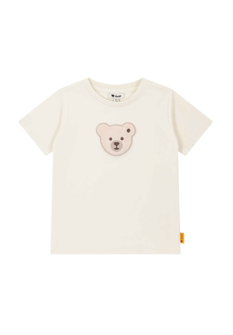 Camiseta de algodón crema con un suave parche bordado de la cara de un oso en marrón claro y marrón oscuro en el pecho. Mangas cortas y escote redondo.