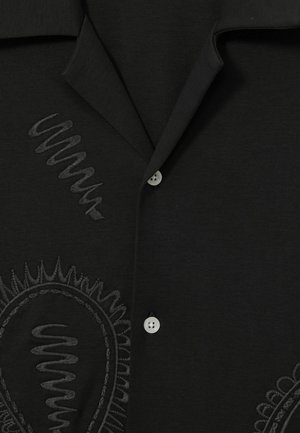 Black shirt featuring a textured pattern with embroidered swirls and circular designs, complemented by white buttons. Soft fabric, collared design.
