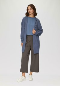 Hellblauer, gerippter langer Cardigan mit Kapuze und Taschen, kombiniert mit einem passenden kurzärmeligen Oberteil und grauen weit geschnittenen Hosen, ergänzt durch weiße Sneakers.