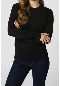 Maglione nero a maglia con collo rotondo, polsini e orlo a coste. Presenta sottili maniche a sbuffo. Indossato con jeans blu scuro.