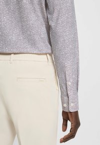 Camicia a maniche lunghe con un motivo a pois viola e bianchi; pantaloni bianchi con una consistenza liscia e un logo sottile sulla tasca posteriore.