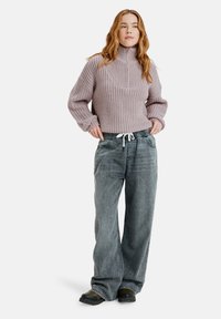 Un pull en tricot lilas clair avec un col montant, associé à un pantalon en denim gris ample avec une taille élastique et des poches avant.