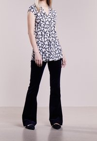 Blus med blommönster och korta ärmar, marinblå bakgrund, vita blommor; matchad med svarta sammetsbyxor med vida ben och svarta loafers.