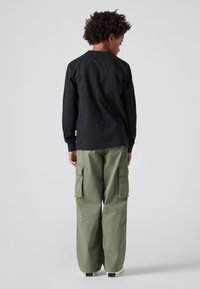 Μαύρο μακρυμάνικο μπλουζάκι συνδυασμένο με ελαιόχρωμα cargo παντελόνια με πλαϊνές τσέπες, χαλαρή εφαρμογή και μανσέτα, απεικονιζόμενο από πίσω.