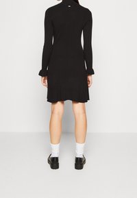 Musta resorimekko, jossa pitkät hihat, röyhelöidyt hihansuut ja hillitty takayksityiskohta. Yhdistetty valkoisiin sukkiin ja mustiin korotettuihin kenkiin.