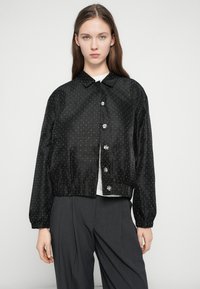 Čierna skrátená bunda zo saténu s bielymi bodkami, s golierovým výstrihom, zapínaním na gombíky a elastickým lemom a manžetami.