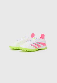 White soccer cleats with green outsole, pink accents, and stripe design. Textured upper with lacing system and padded heel area.
