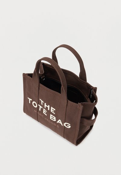 Hnedá plátnená taška s dvojitými uchami, vonkajšími vreckami a potlačou "THE TOTE BAG MARC JACOBS" na prednej strane.
