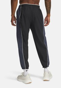 Schwarze Trainingshose mit einem strukturierten maritimen Panel, elastischem Bund, weißen Seitenstreifen und elastischen Bündchen, kombiniert mit weißen Sneakers.