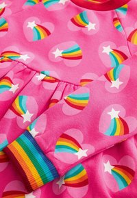 Pink fabric with heart patterns containing white stars and rainbow trails, featuring a ribbed sleeve cuff with rainbow stripes.