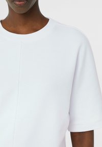 Biały bawełniany sweatshirt z krótkimi rękawami, okrągłym dekoltem i widocznymi detalami szwów, charakteryzujący się gładką teksturą i luźnym fasonem.