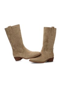 Botas de ante beige de estilo western con punteras puntiagudas y tacones bajos, que presentan tachuelas metálicas decorativas en los laterales.