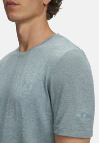 Heled sinine sportlik T-särk, mis on valmistatud tekstureeritud kangast, ringkäe, lühikeste varrukate ja diskreetse logoga rinnal ja varrukal.
