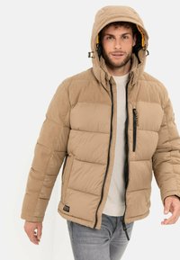 Beige Pufferjacke mit geripptem Stoff an den Schultern, verstellbare Kapuze, frontaler Reißverschluss und Seitentaschen; strukturierter Stoff und entspannter Schnitt.